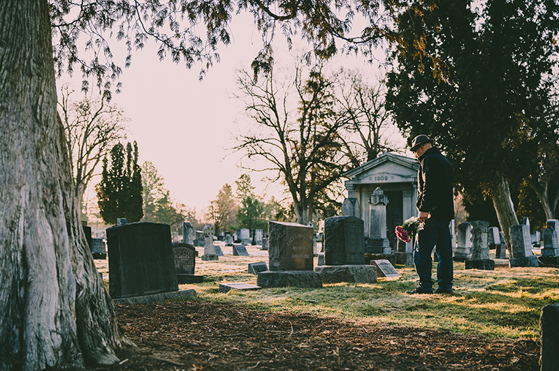 一位手拿花束的男人走到墓碑前準備悼念他的親人